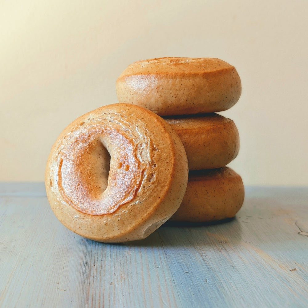 Four gluten-free plain bagels stacked on a blue wooden surface
