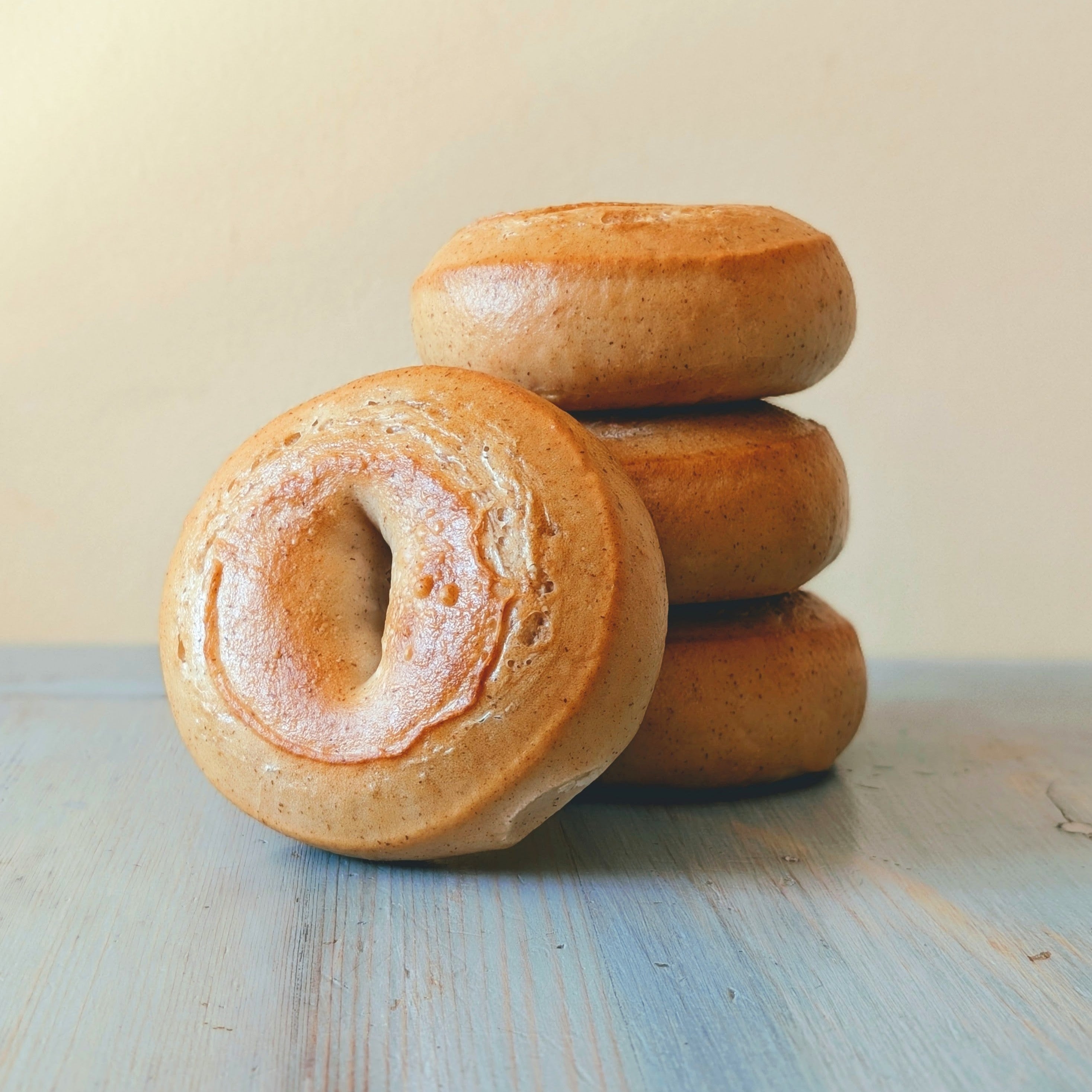 Four gluten-free plain bagels stacked on a blue wooden surface