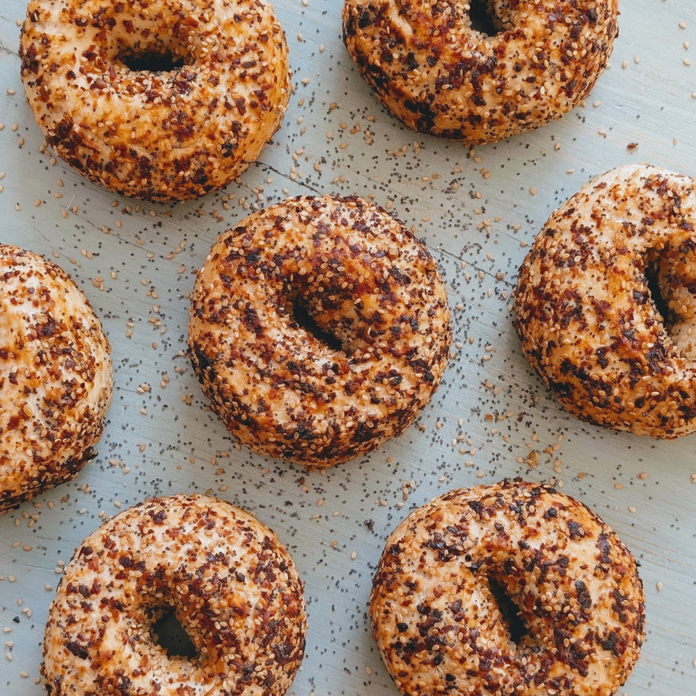 Toasted everything-style bagels with sesame and seasoning scattered on pale blue wooden surface