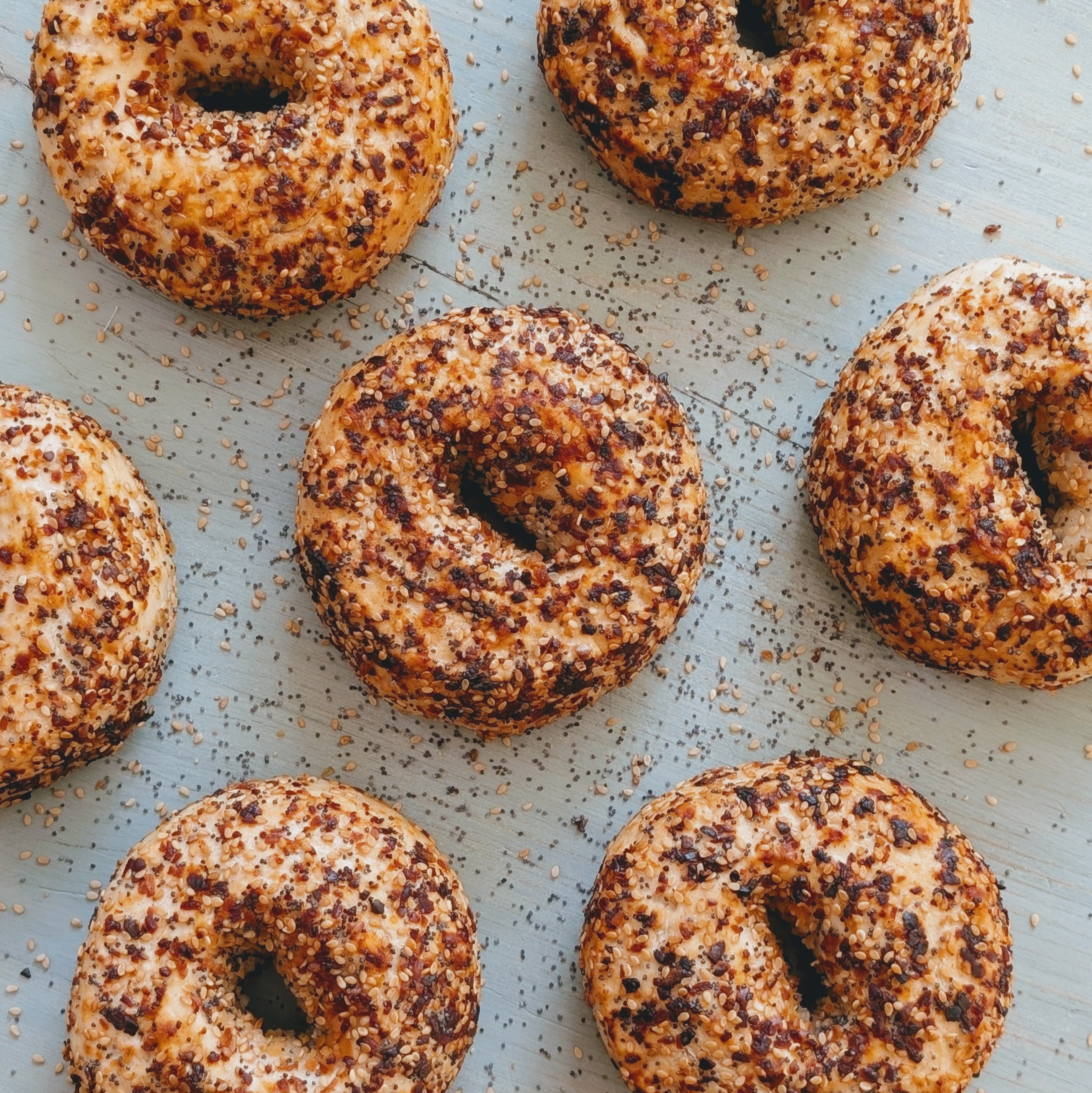 Toasted everything-style bagels with sesame and seasoning scattered on pale blue wooden surface