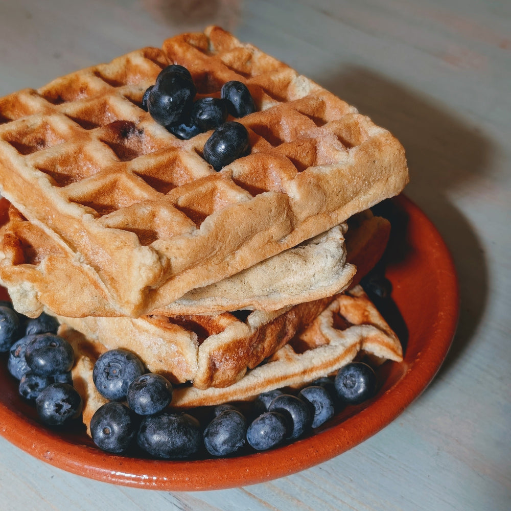 Stacked golden waffles on a red plate topped and surrounded by fresh blueberries