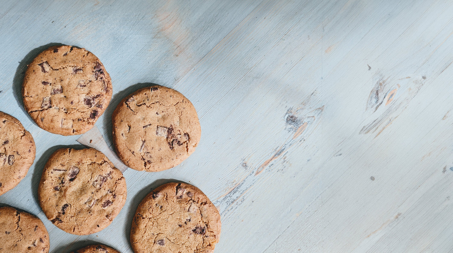 Chocolate-chip cookies scattered along the left on a pale blue wooden surface