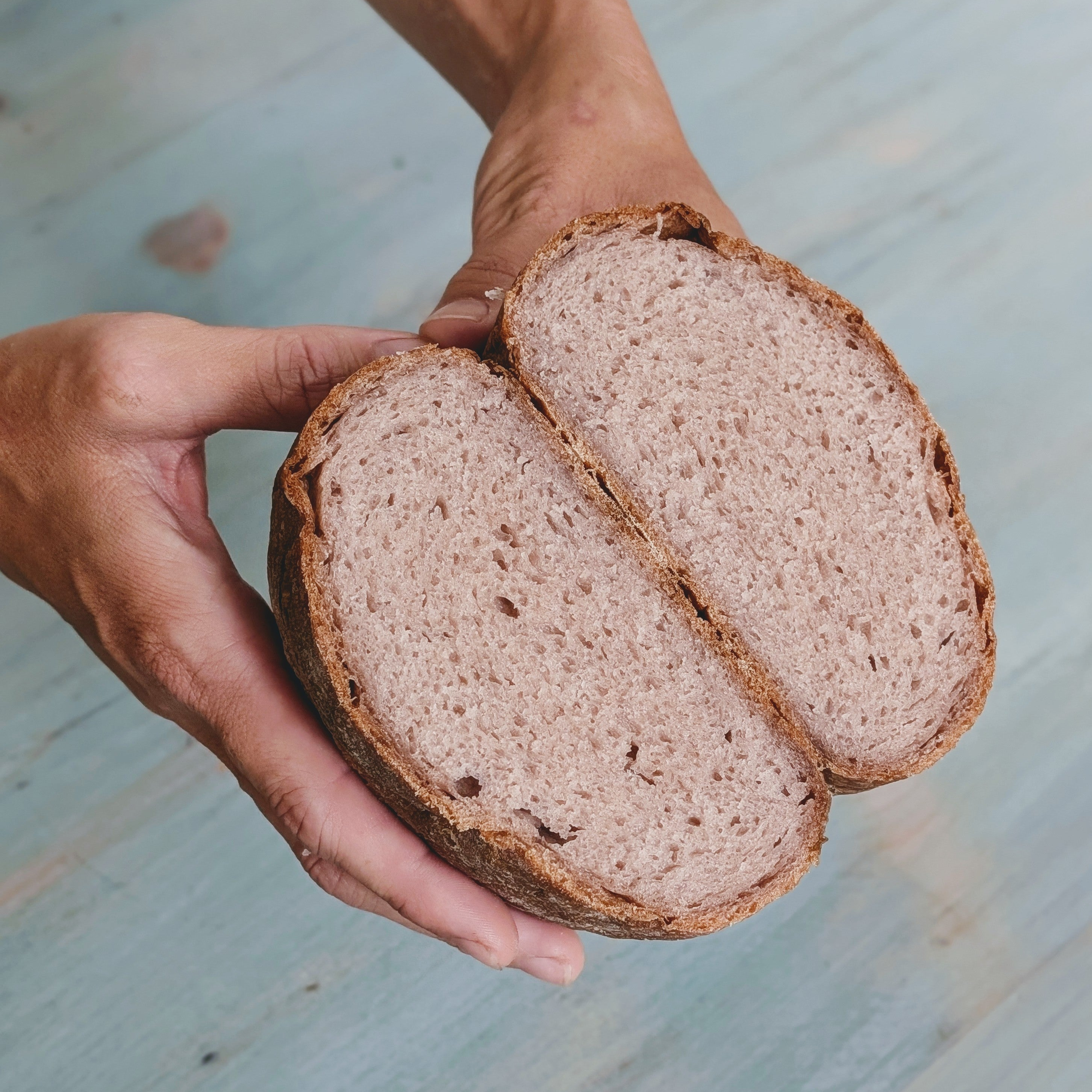 A person holding a sliced gluten-free country loaf showing its interior texture.