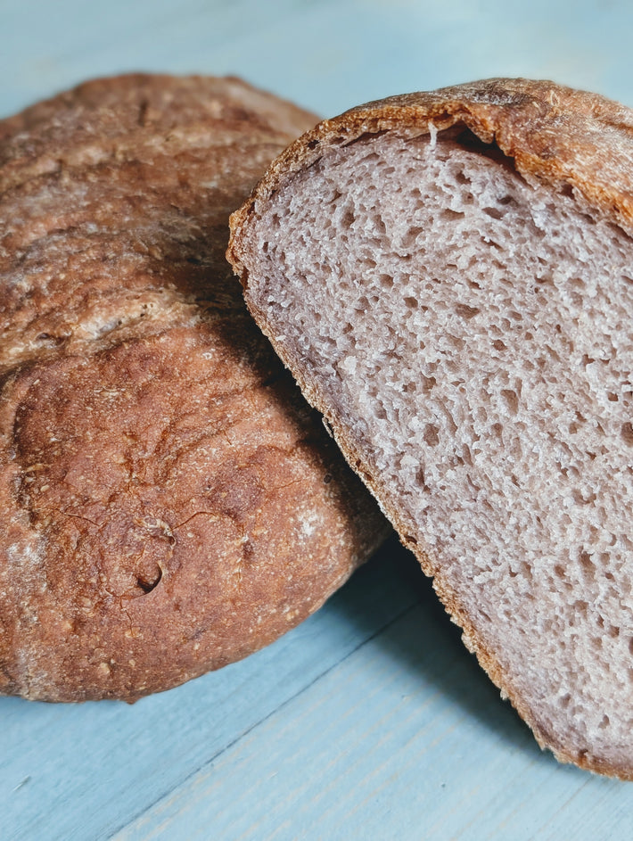 Gluten-Free Country Loaf, partially sliced to show soft interior, on a light blue surface.