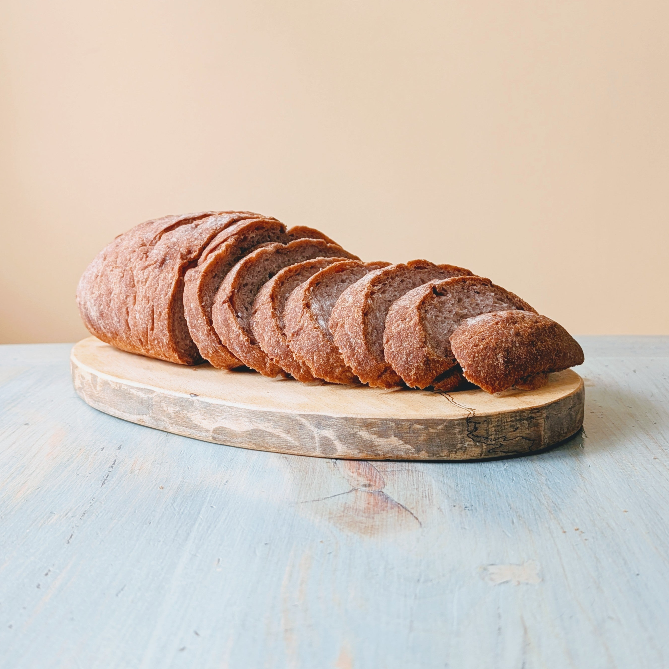 Sliced rustic whole-grain loaf on a round wooden cutting board atop a light blue tabletop.