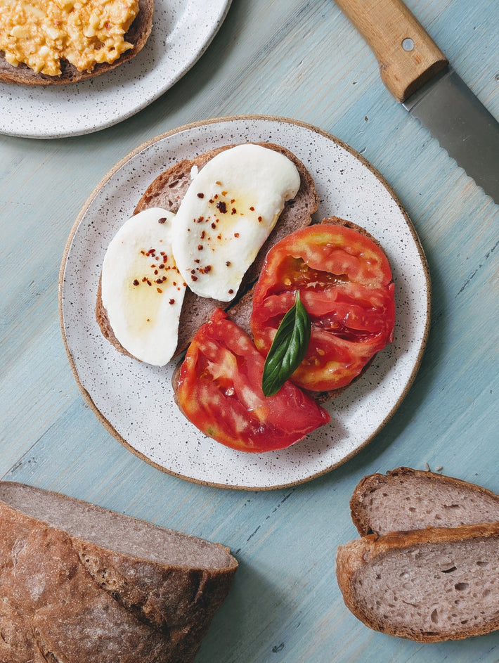 Sliced brown bread with fresh mozzarella, tomatoes, and basil on a plate.
