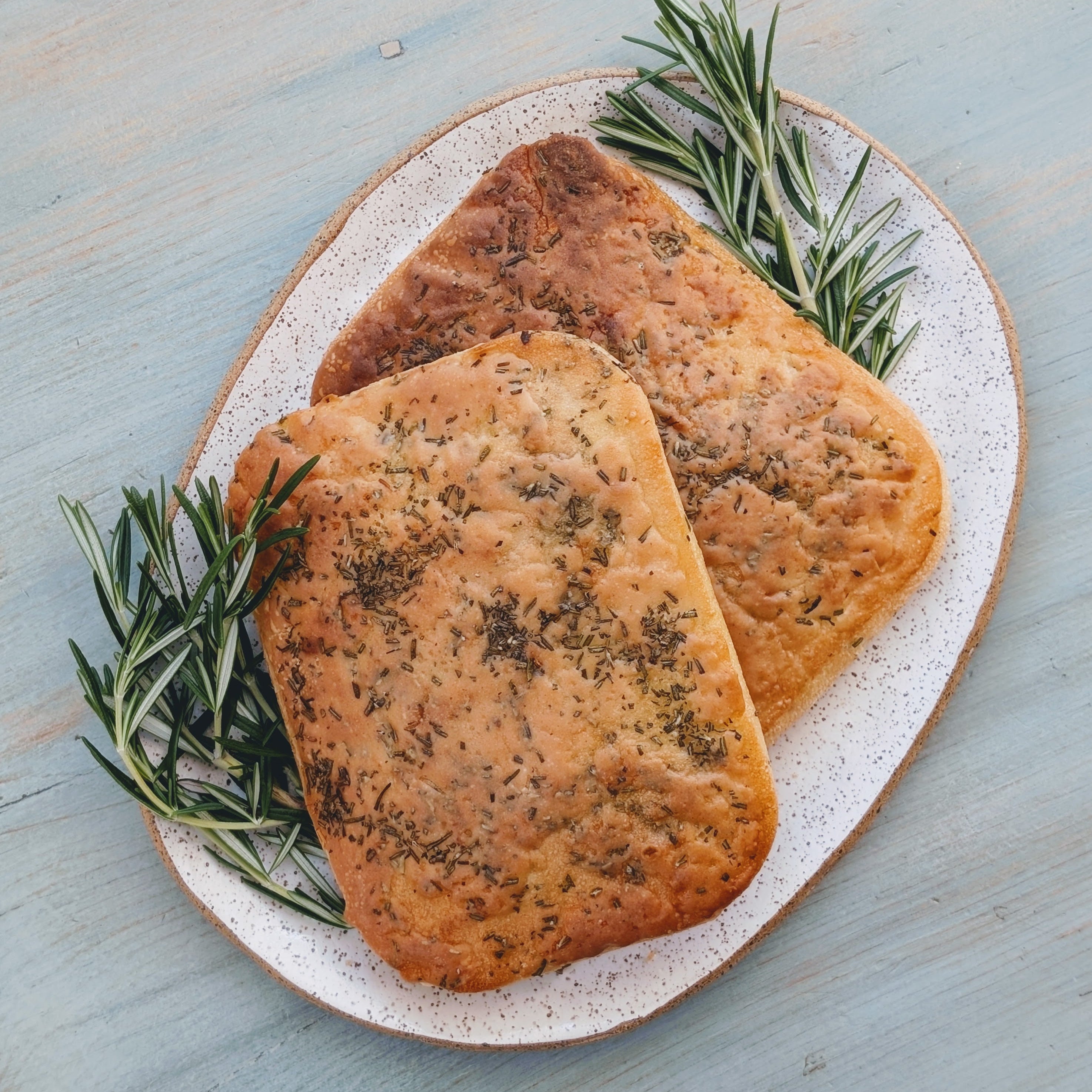 Two pieces of Wildgrain gluten-free focaccia bread garnished with rosemary on a plate.