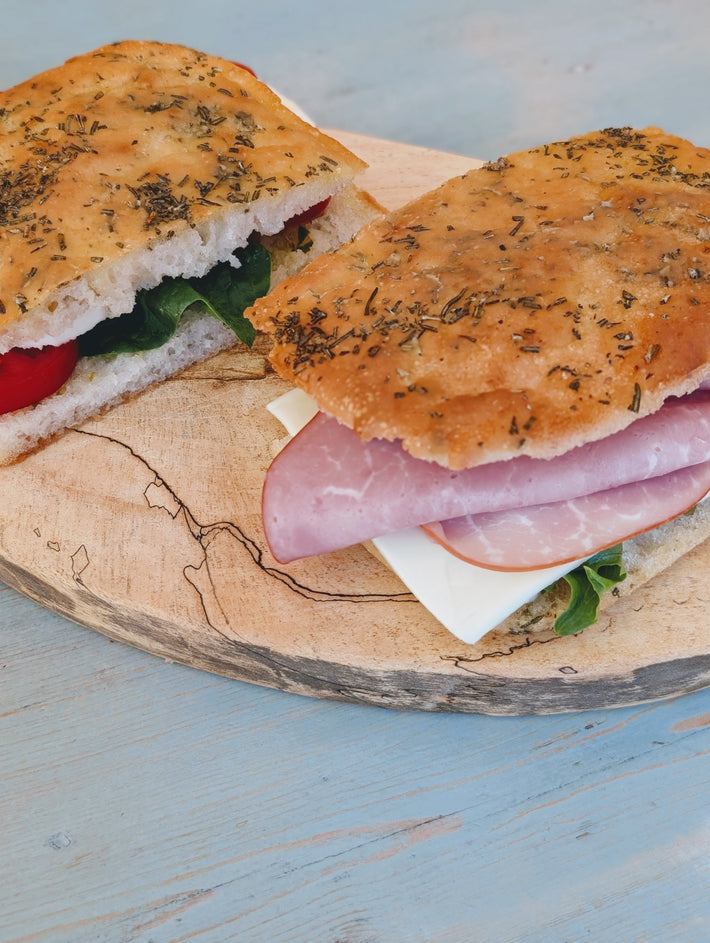 Focaccia sandwich with ham, sliced cheese and greens on a round wooden board