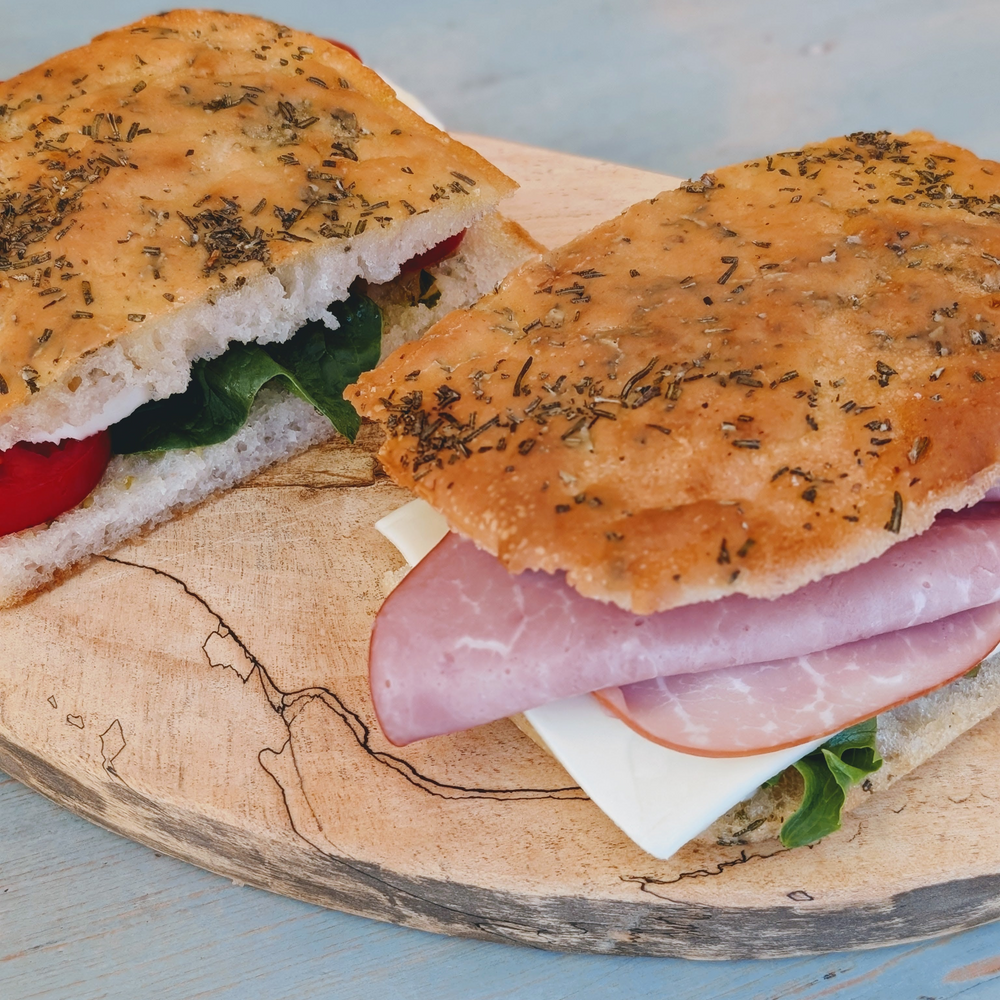 Focaccia sandwich with ham, cheese, lettuce and tomato on a wooden cutting board