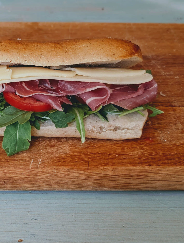 Submarine sandwich with deli meats, cheese, and vegetables on a wooden cutting board.