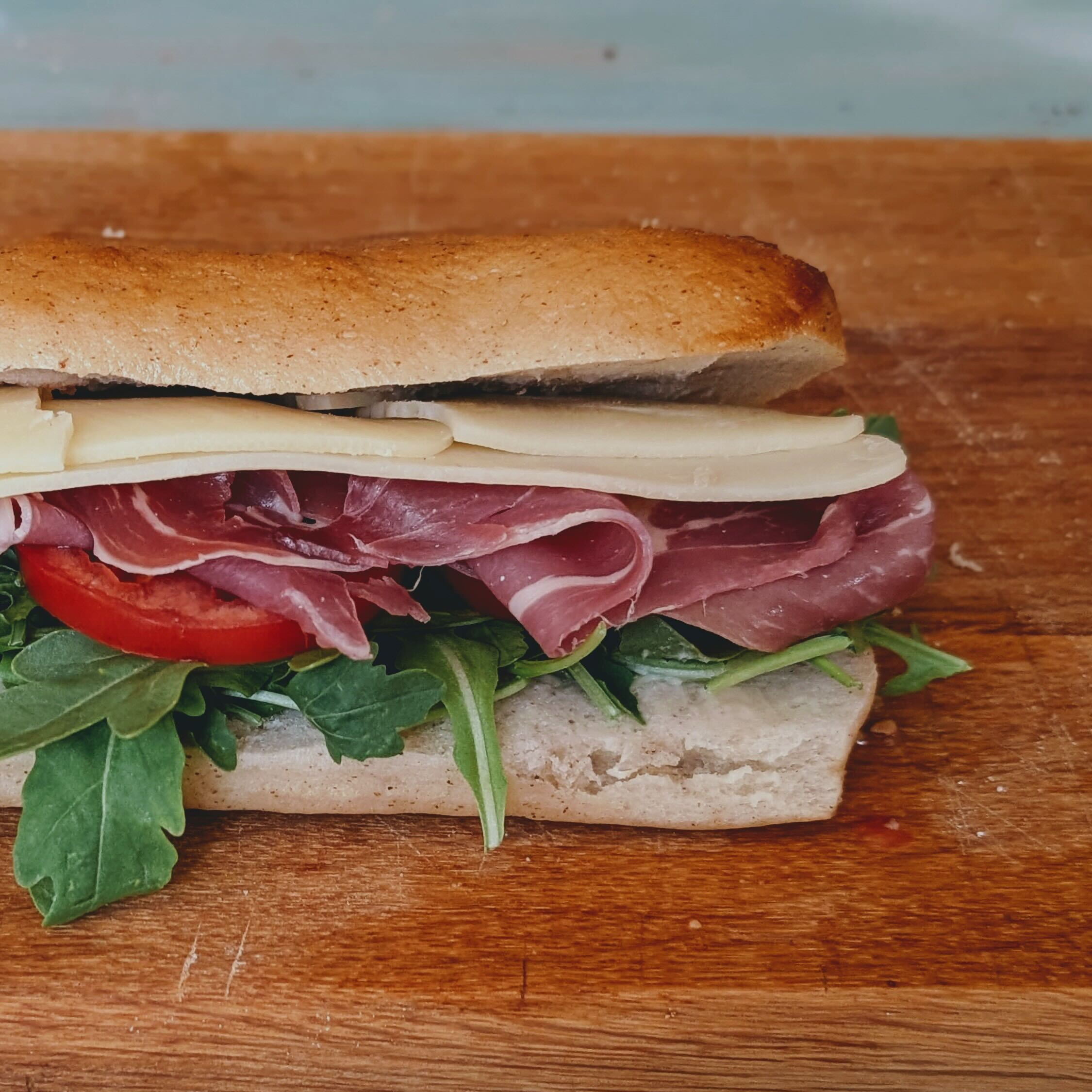 Ciabatta sandwich with prosciutto, provolone, arugula and tomato on a wooden cutting board.
