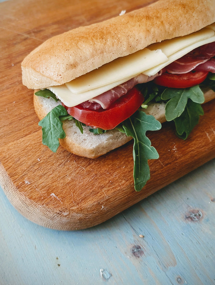 Submarine sandwich with cheese, tomatoes, and arugula on a wooden cutting board.