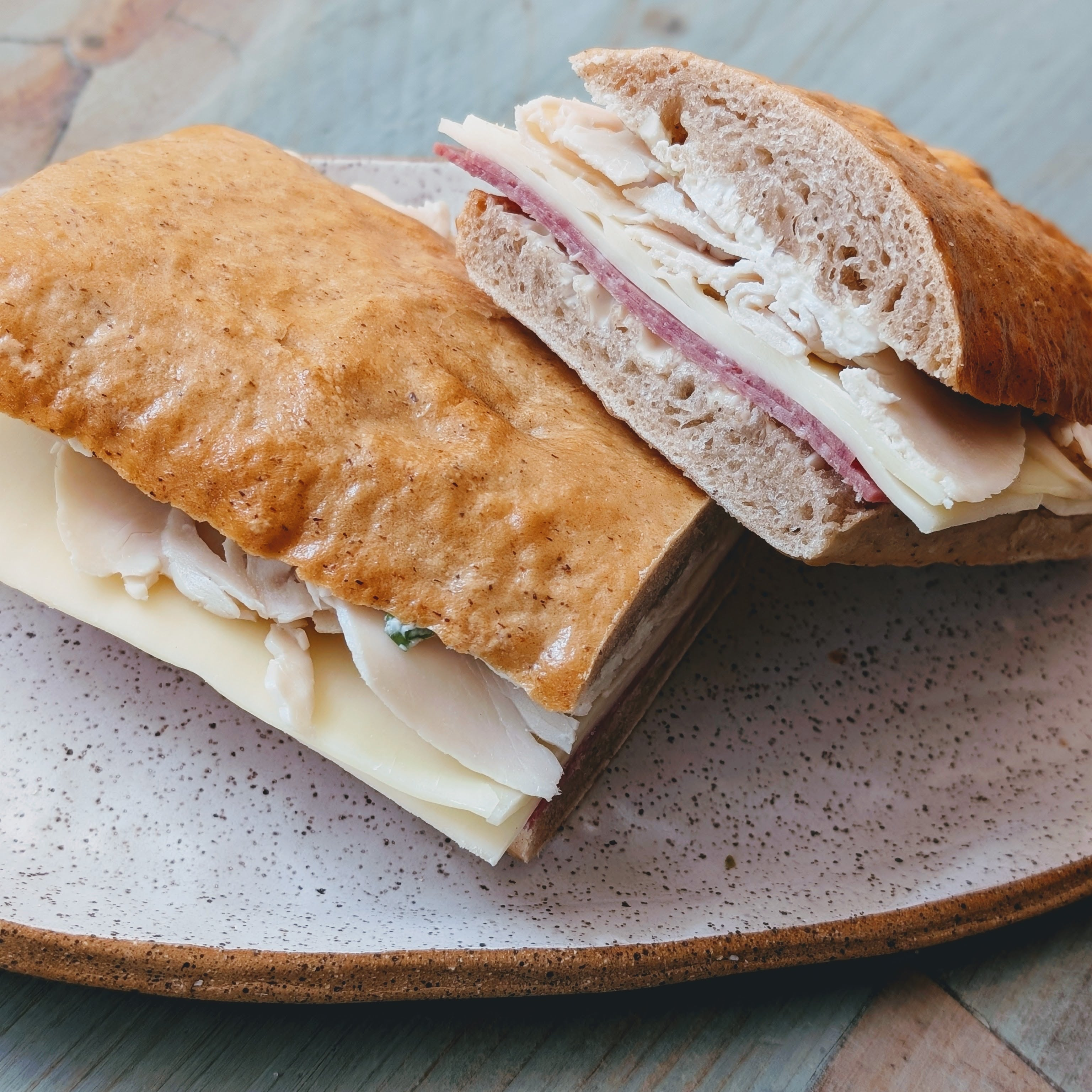 Ciabatta sandwich halves with sliced turkey, salami, and Swiss cheese on a speckled ceramic plate