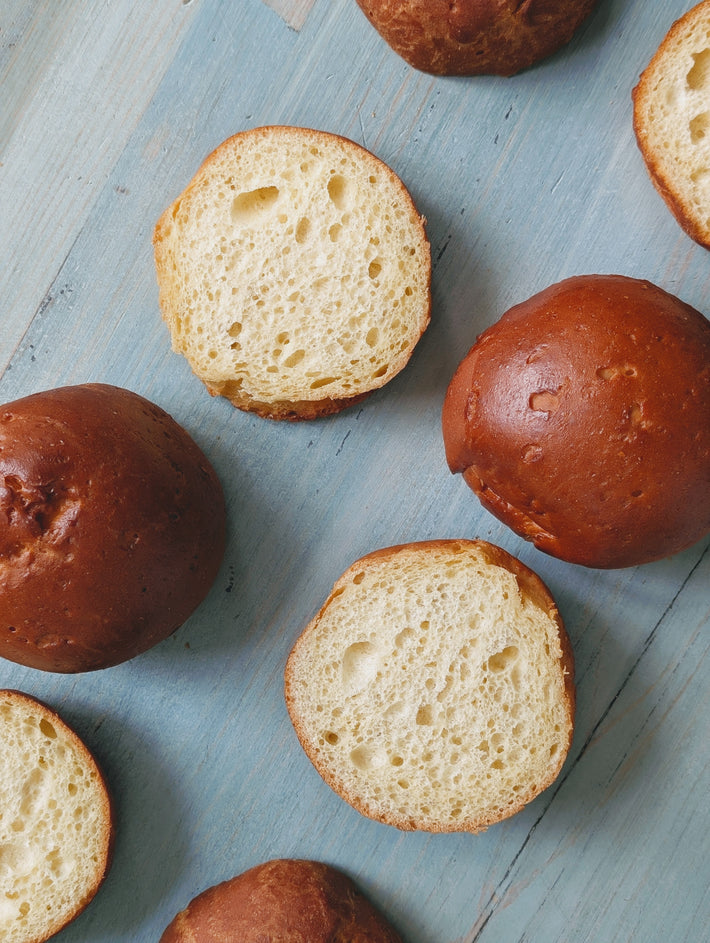 Gluten-Free Slow-Fermented Brioche Rolls displayed on a light blue wooden surface, some cut in half to show the soft interior.