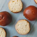 Top view of Gluten-Free slow-fermented brioche rolls (4-pack) showing golden-brown crust and airy interior on light blue wood