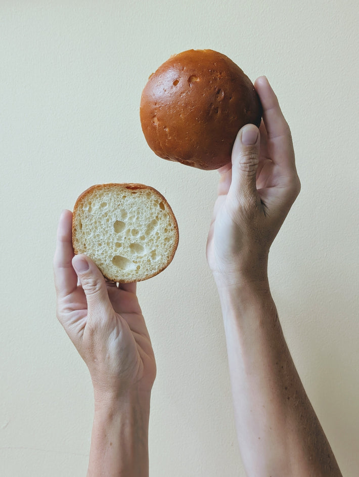 Hands holding a brioche roll and its sliced half, showing the airy interior crumb.