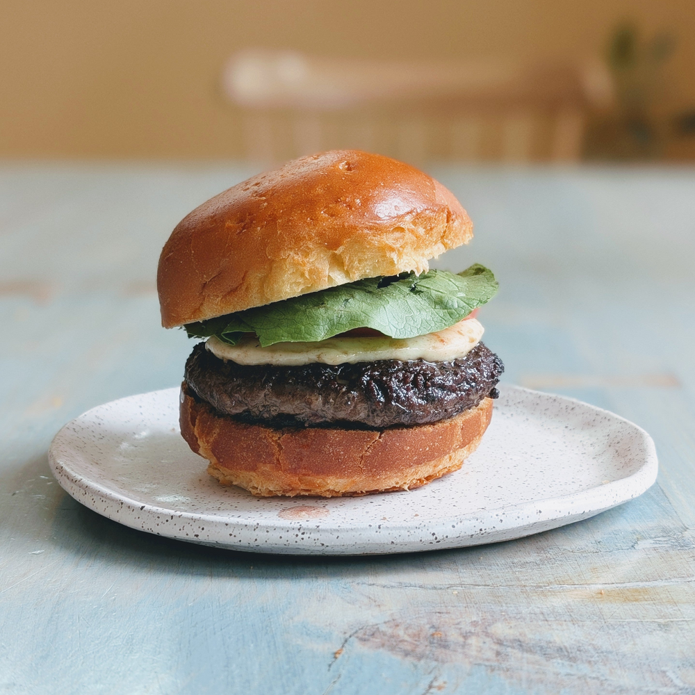Brioche roll sandwich with beef patty, lettuce and sauce on a speckled white plate