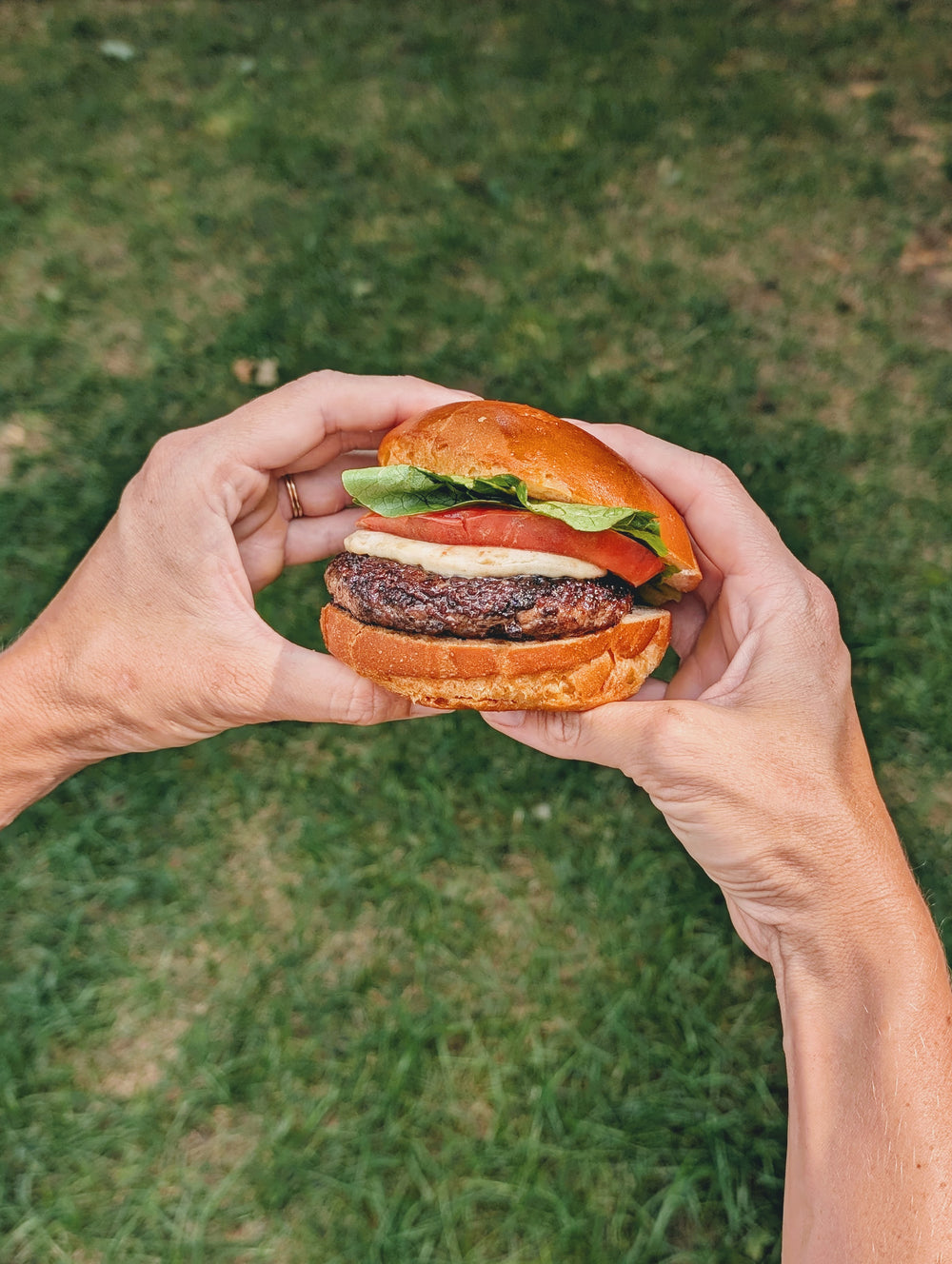 Close-up of gluten-free slow-fermented brioche roll used as burger bun showing golden crust and soft interior against grass