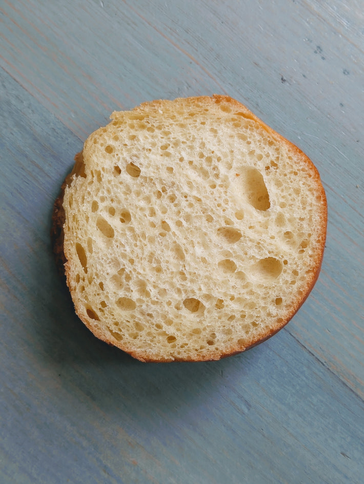 Slice of brioche roll with airy crumb and golden crust on a blue wooden surface.