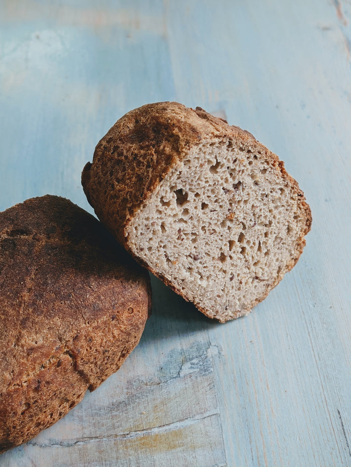Partially sliced rustic bread showing a textured interior on a light blue wooden surface.