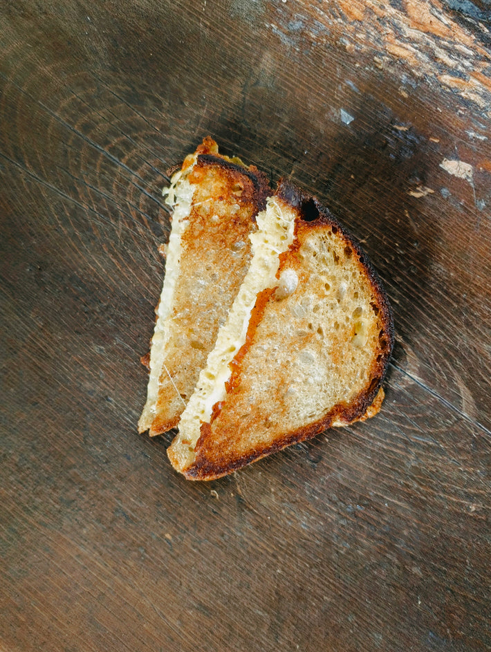 Grilled cheese sandwich cut in half with melted cheese on toasted sourdough, placed on a worn wooden surface.
