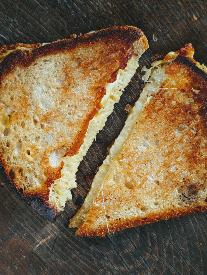 Grilled cheese sandwich cut in two on a dark wooden board, golden toasted bread and melted cheese stretching between halves