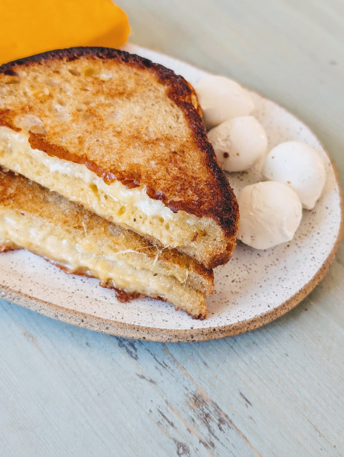 Grilled cheese sandwich cut in half on a speckled plate with small butter scoops, on a pale blue wooden table.