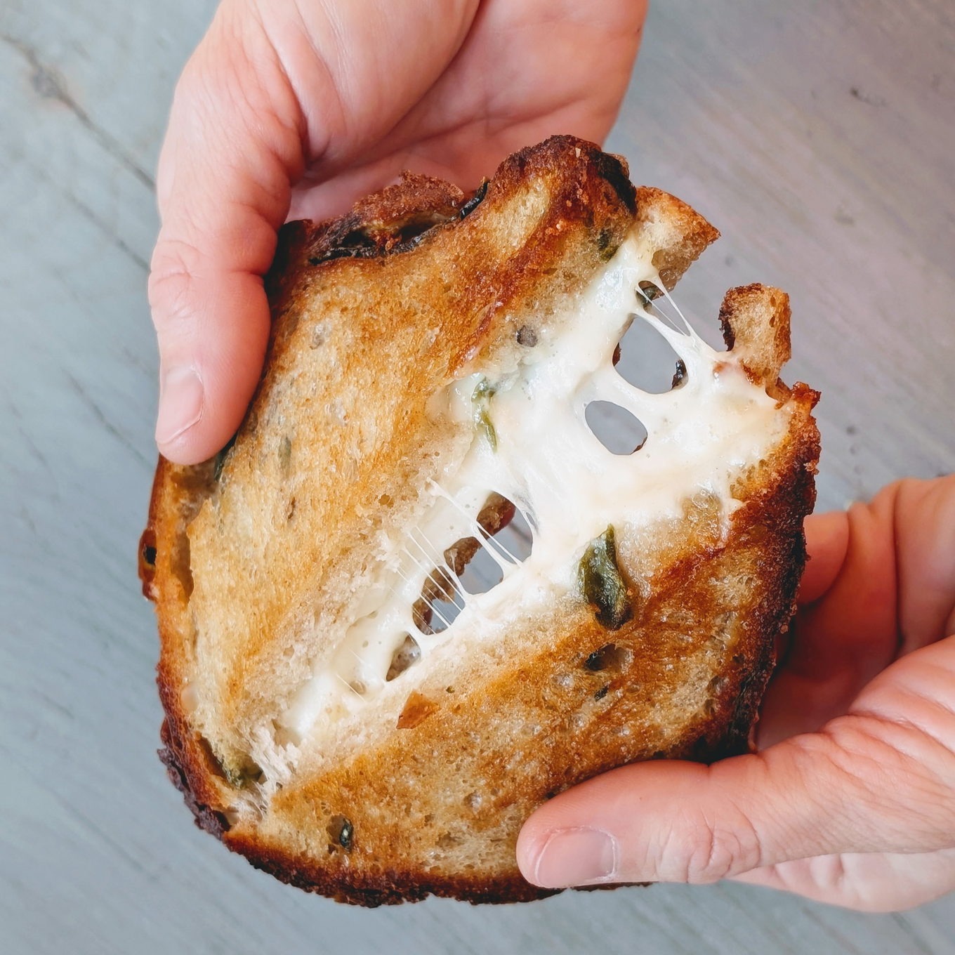 Hands pulling apart a toasted grilled cheese sandwich, showing stretchy melted cheese between crispy rustic bread.
