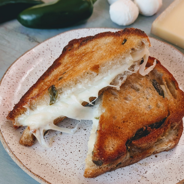 Three-quarter view of sourdough jalapeño grilled cheese with gooey Gruyère and mozzarella and visible jalapeño slices on a speckled ceramic plate