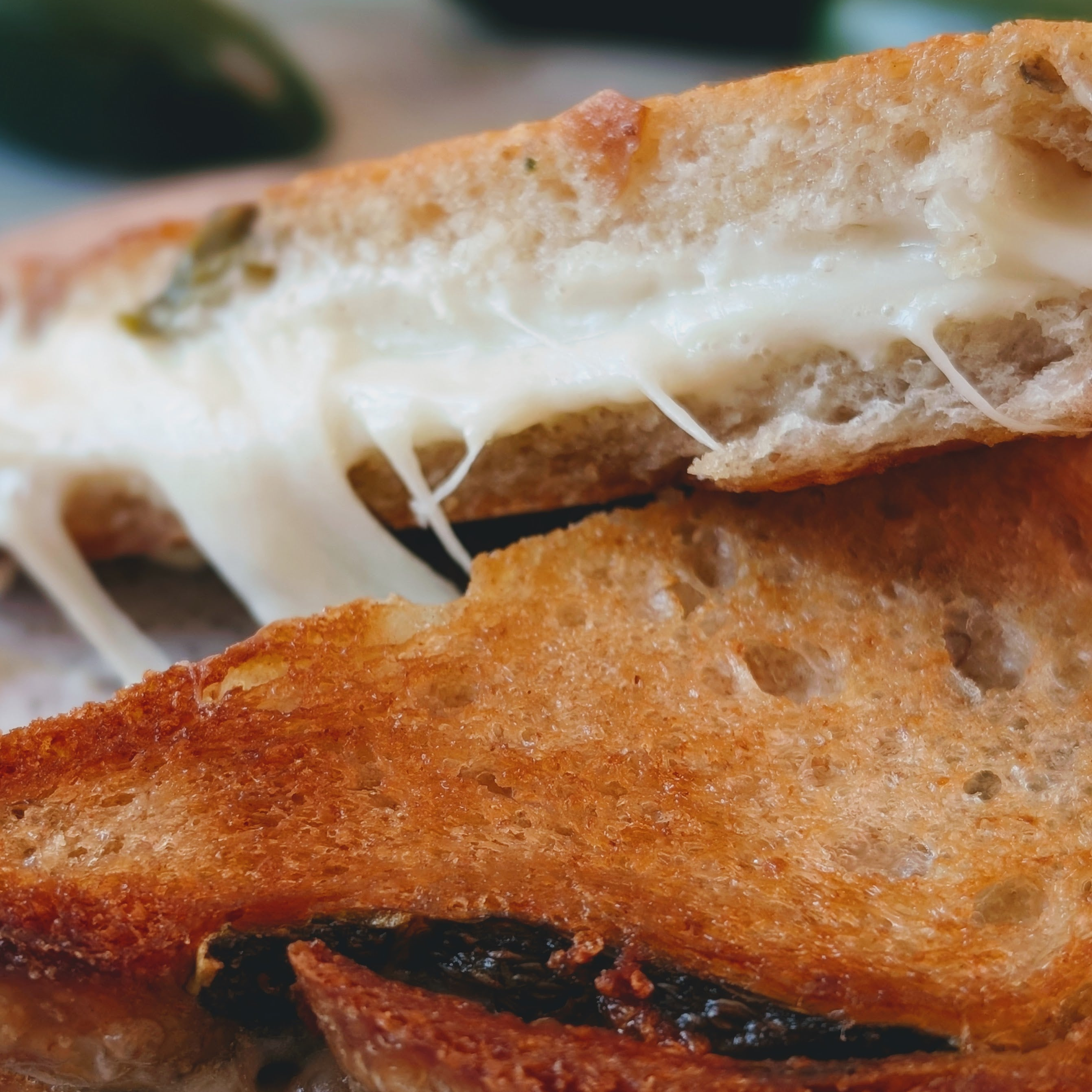 Close-up of toasted grilled cheese sandwich with melted, stringy cheese between golden-brown bread slices