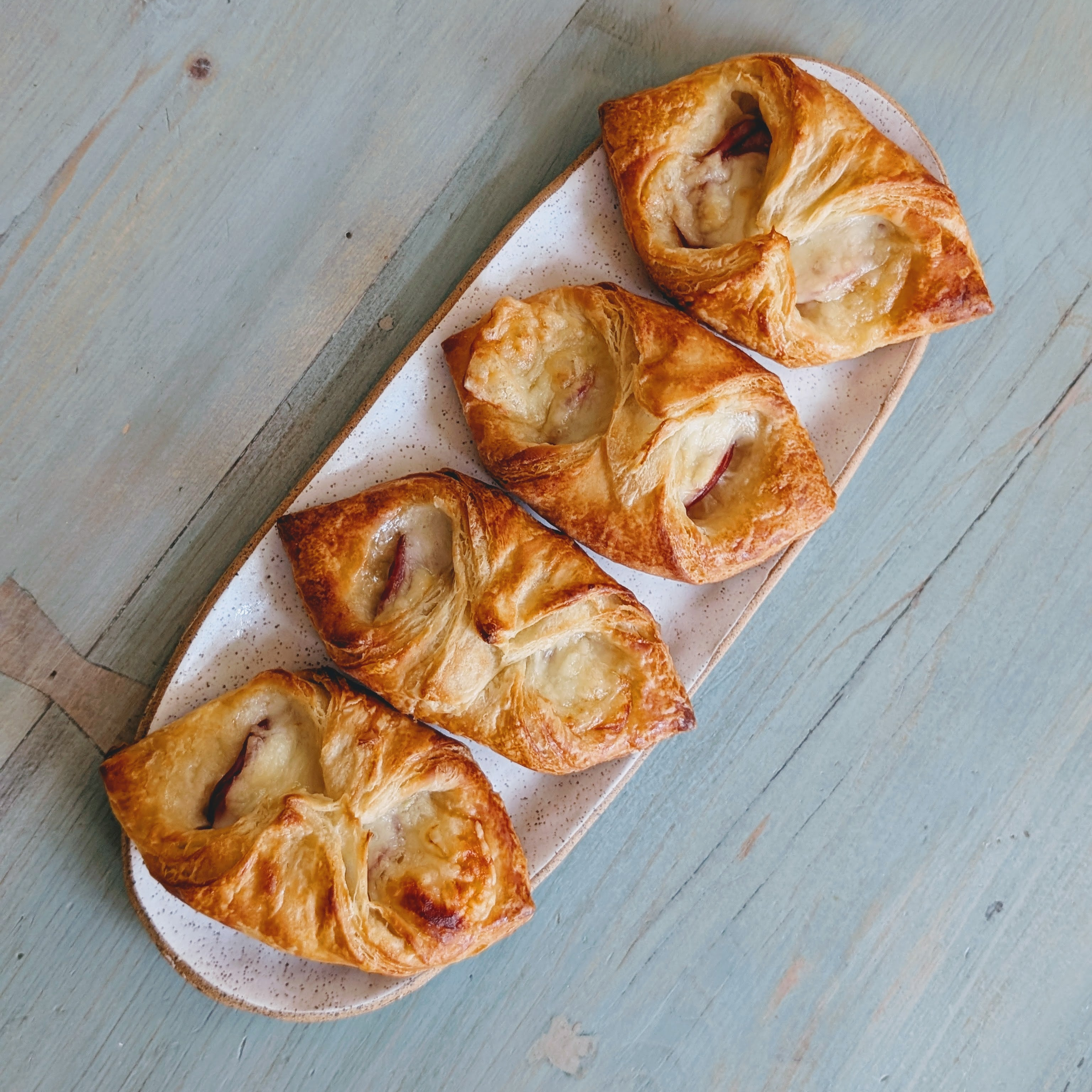 Four golden puff pastries with melted cheese on a speckled oval plate, top-down on a weathered blue wooden table.