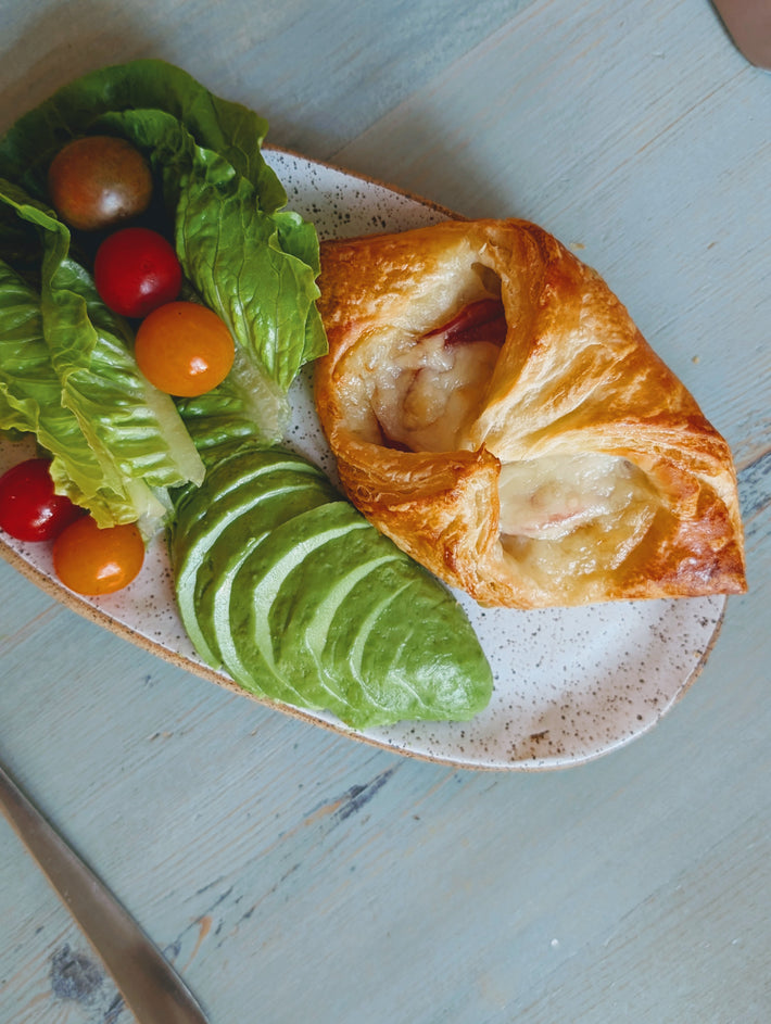 Ham & Cheese Croissant with avocado, lettuce, and cherry tomatoes on a plate.