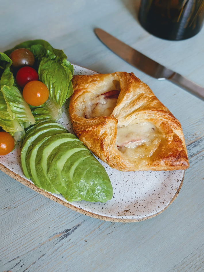 Ham & Cheese Croissant on a plate with avocado, lettuce, and cherry tomatoes.