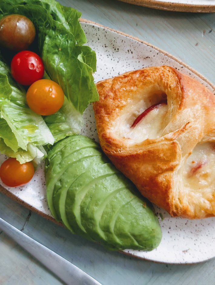 Flaky pastry with cheese and fruit, served with avocado, lettuce, and cherry tomatoes.