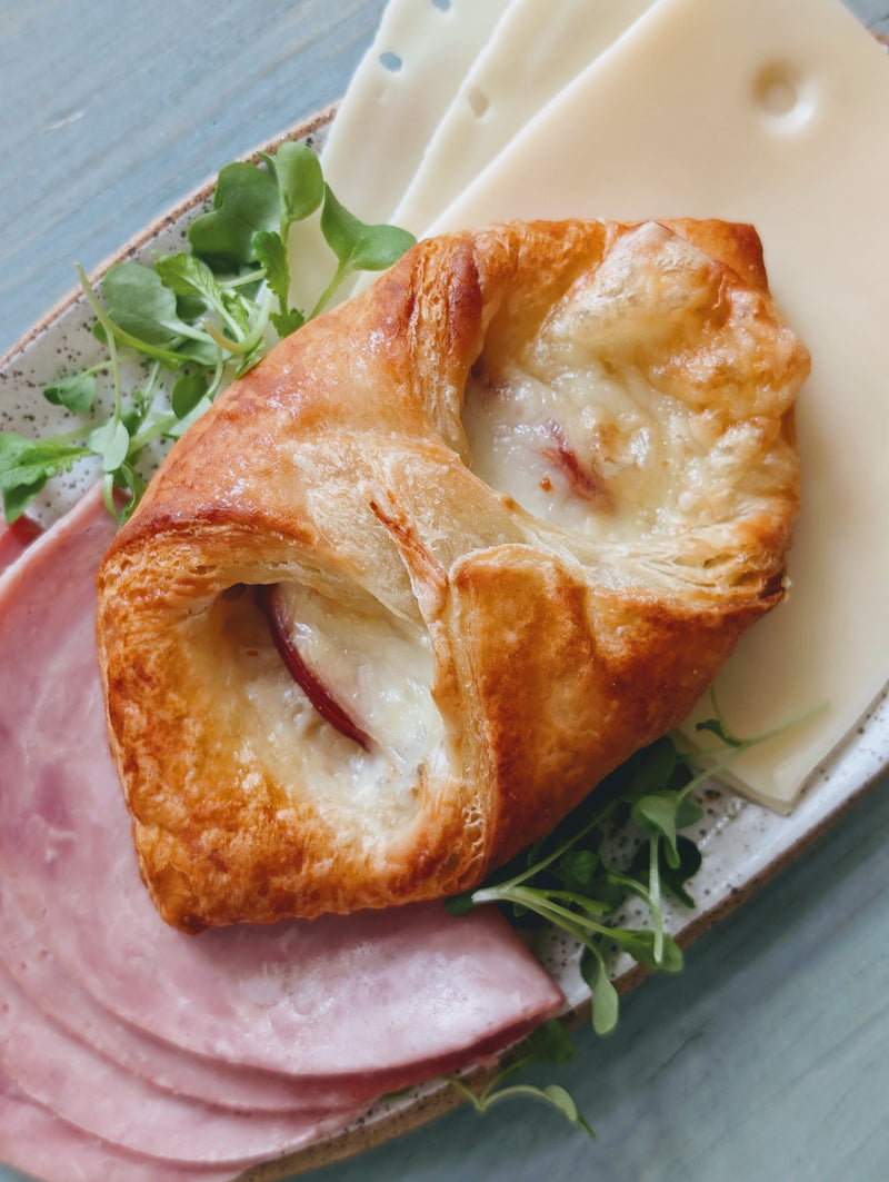 Top-down view of ham and cheese croissant with melted cheese and flaky crust on plate with ham slices and greens