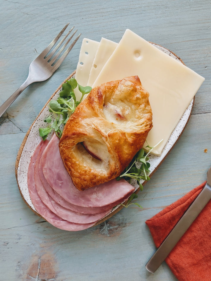 Ham & Cheese Croissants on a plate with sliced ham and cheese, garnished with greens.