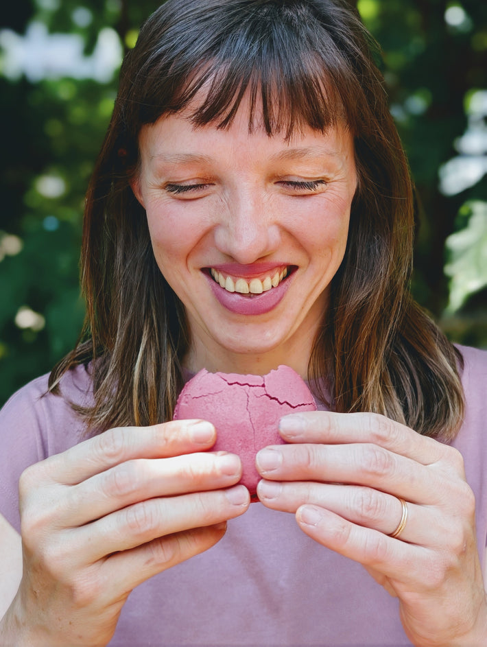 Woman smiling while holding and breaking a pink macaron outdoors