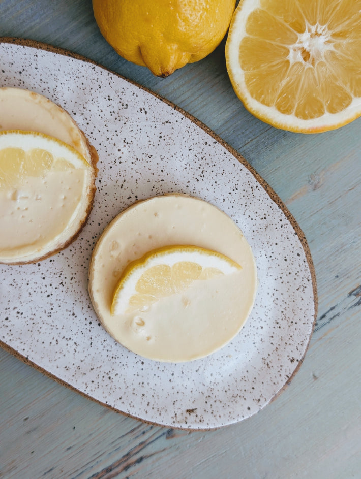 Two Wildgrain Lemon Cheesecake on a speckled ceramic plate with whole lemons in the background.