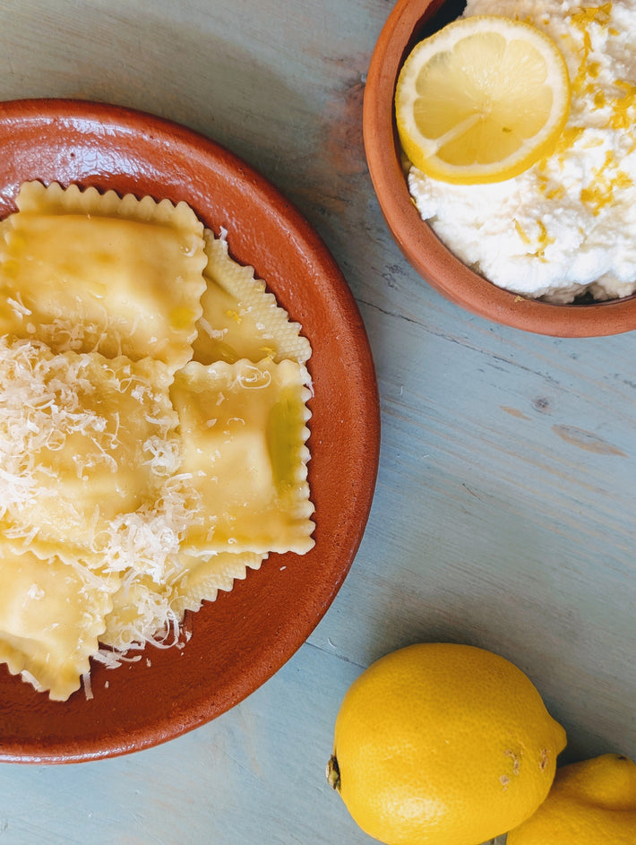 Ricotta and lemon ravioli served with grated cheese, a bowl of ricotta, and fresh lemons.