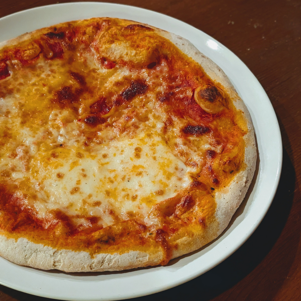 Cheese pizza on a white plate on a wooden table, close-up showing browned crust and melted cheese.