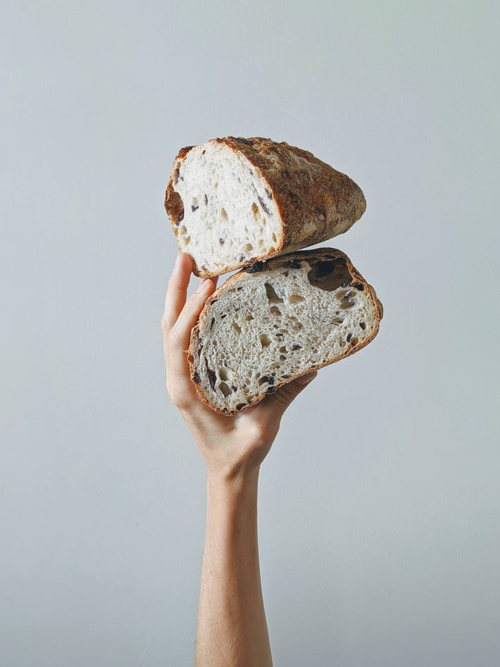 A hand holding a sliced loaf of sourdough bread, showcasing its texture.