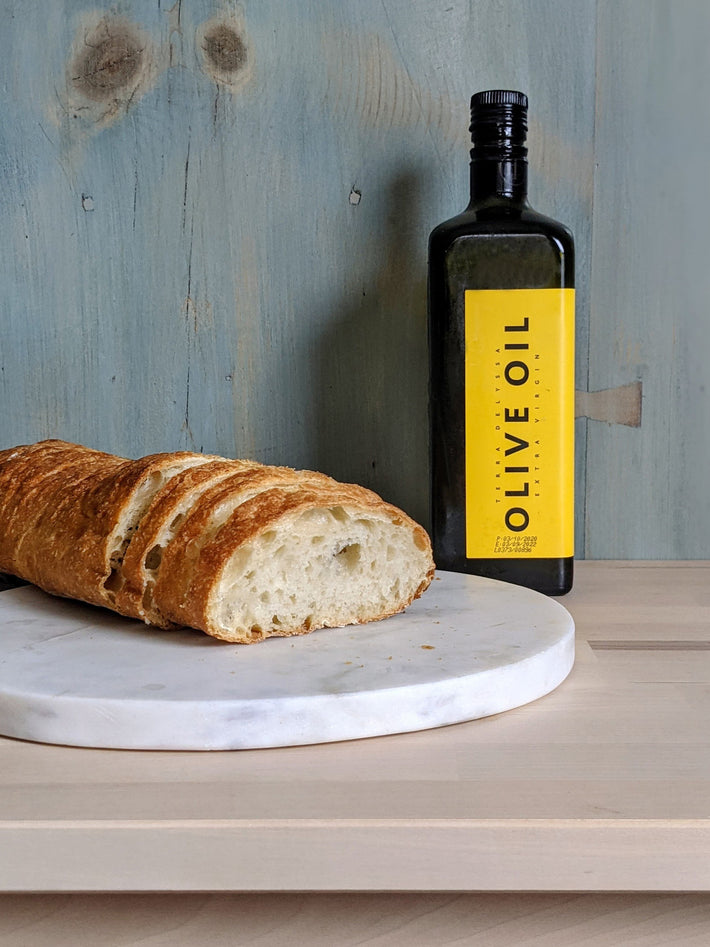 A loaf of ciabatta bread next to a bottle of olive oil with a yellow label
