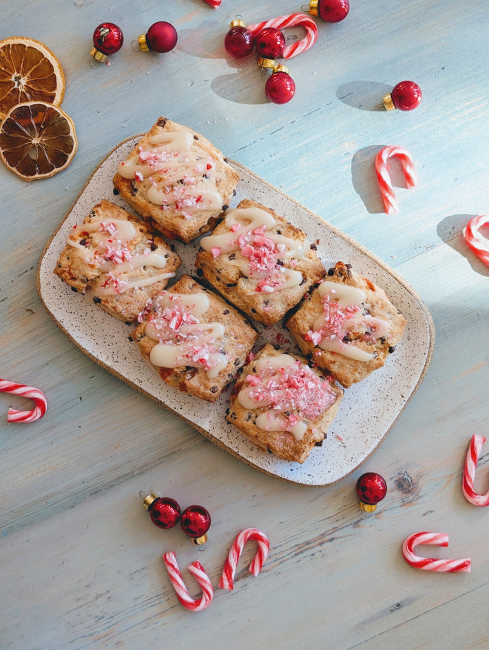 Peppermint-Chocolate Biscuits topped with icing and crushed candy canes on a platter, surrounded by holiday decorations.