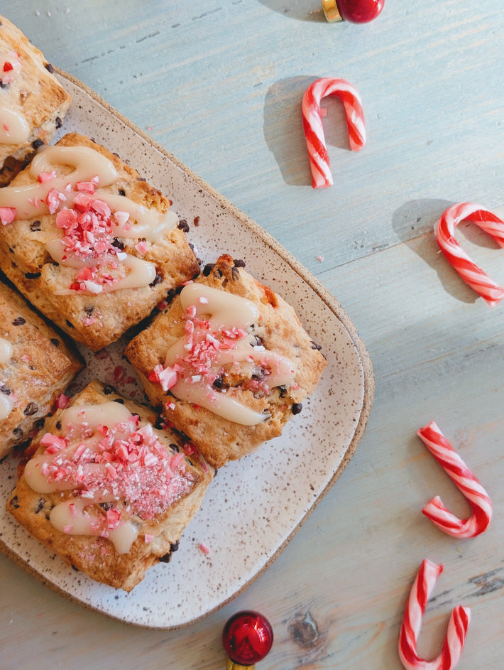 A plate of peppermint-chocolate biscuits topped with icing and crushed candy canes, with candy canes and a red ornament around.