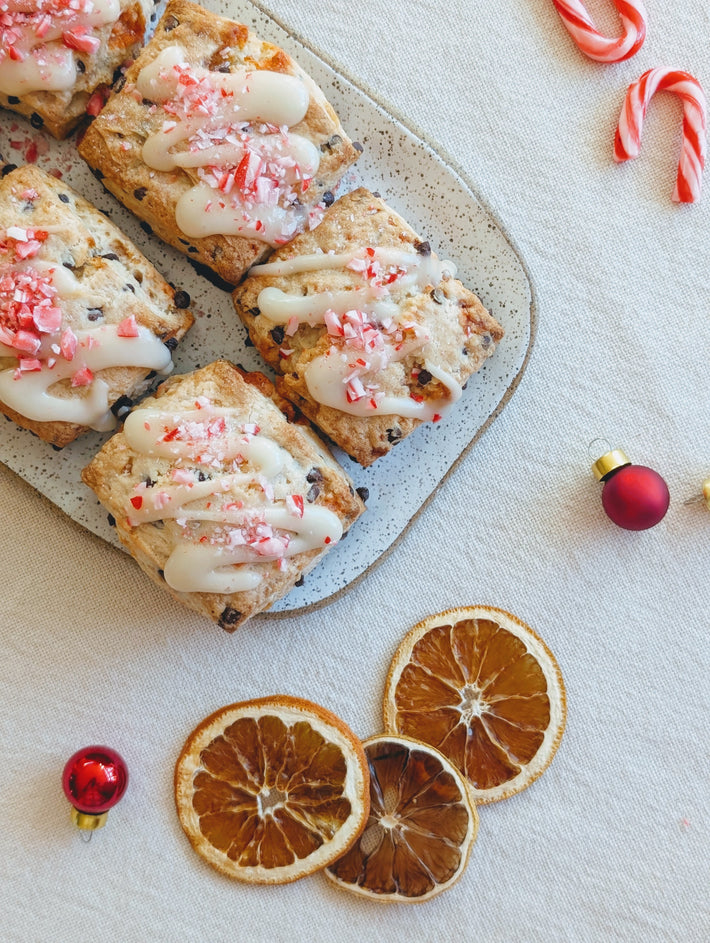Festive pastries with icing and crushed peppermint on a platter, with dried orange slices and holiday decorations.