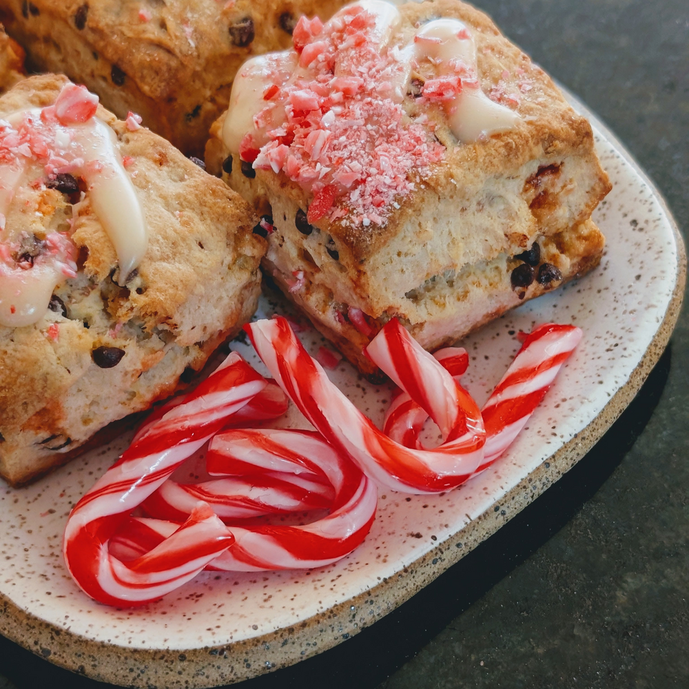 A plate with festive scones topped with crushed peppermint and drizzled icing, alongside red and white candy canes.