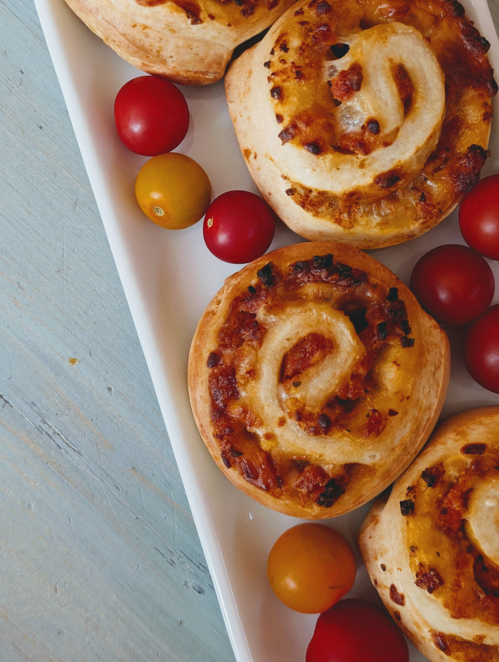 Baked savory pinwheel pastries and red and yellow cherry tomatoes arranged on a white rectangular platter.