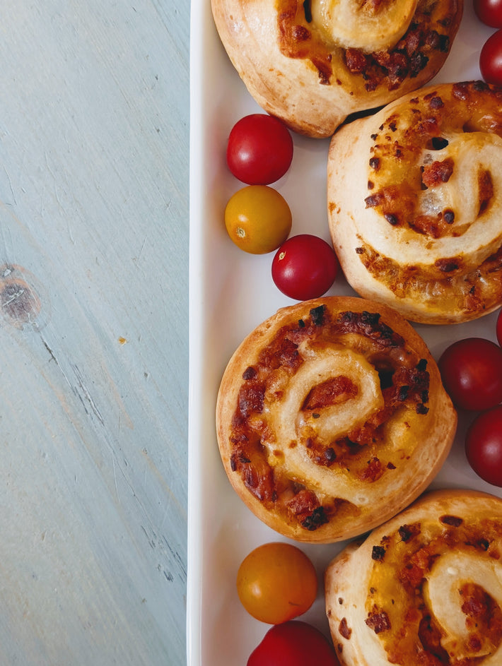 Savory spiral rolls with melted cheese and bacon on a white platter, served with red and yellow cherry tomatoes.
