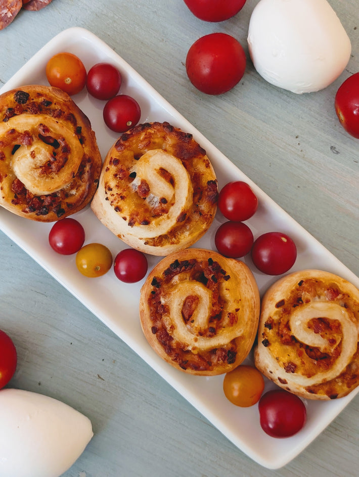 Savory puff-pastry pinwheels with diced tomato and cheese on a white rectangular platter, scattered cherry tomatoes and mozzarella.