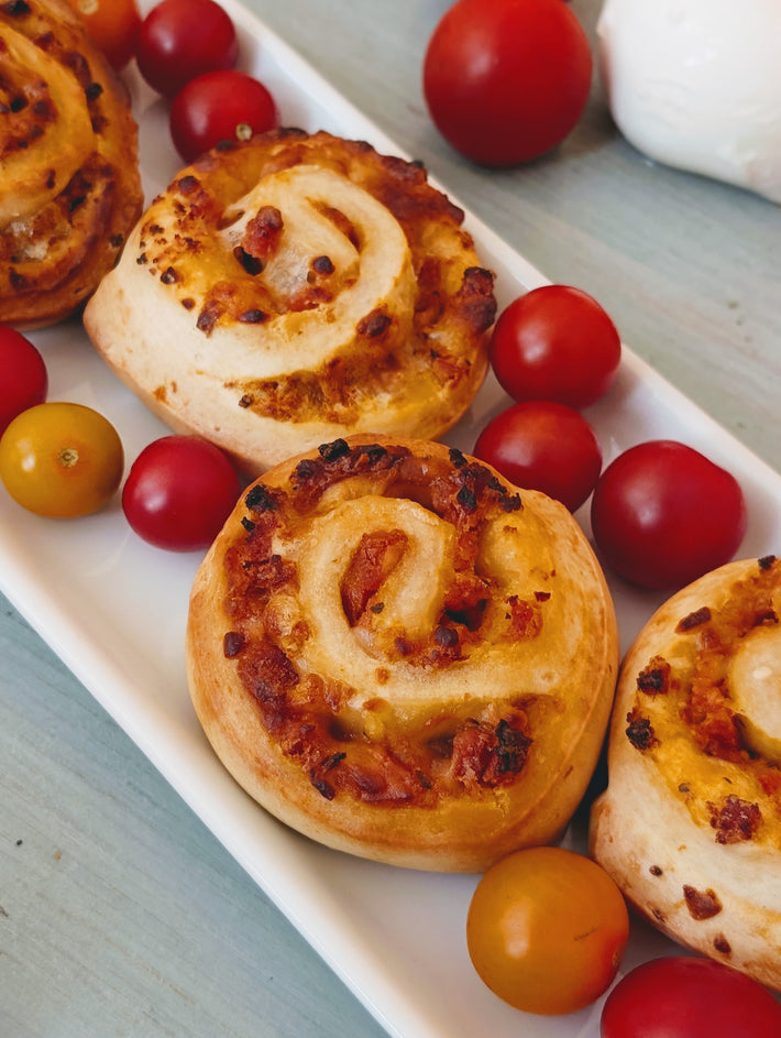 Three baked cheese-and-tomato pinwheel rolls on a white platter with red and yellow cherry tomatoes
